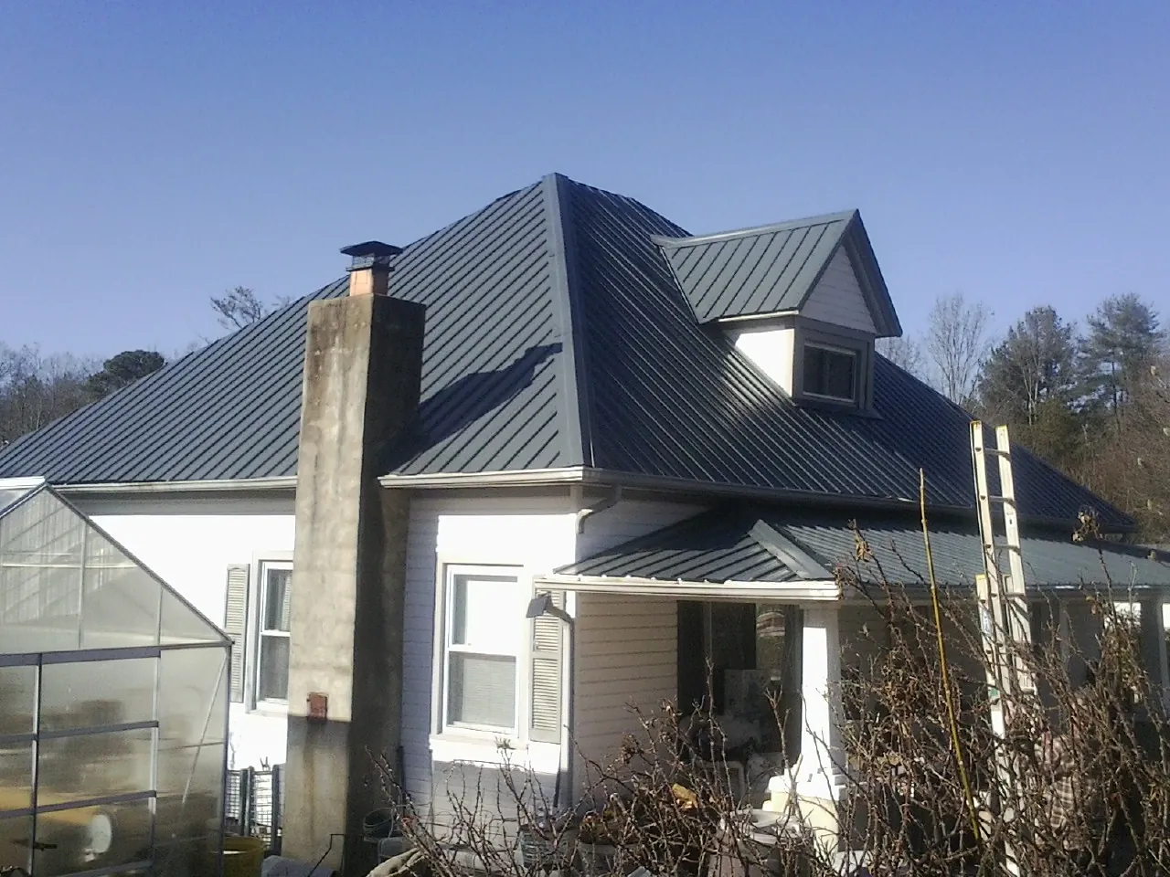 Dark blue standing seam metal roof on a white farmhouse with dormer — Slate & Tile Roof Repair by Roofing Brothers in Petros