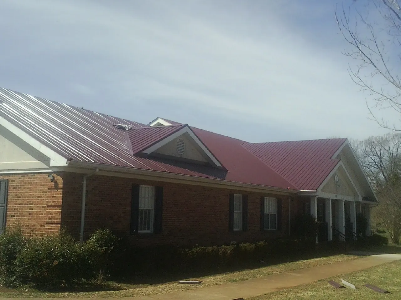 Red metal roof with gabled entries on a long brick building, from a Hail Damage Roof Repair job in Petros