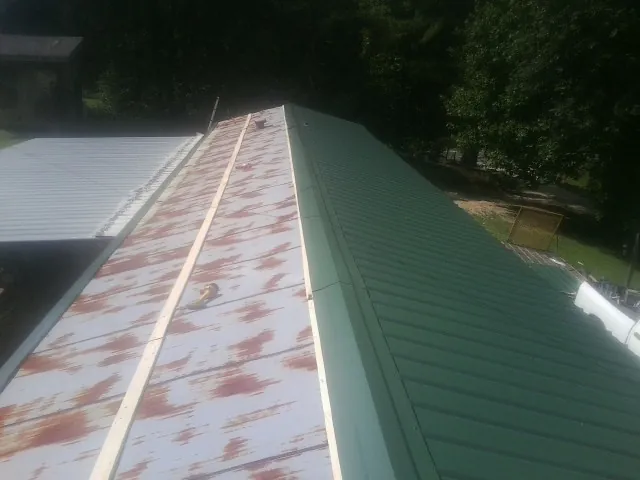 Old rusted panels beside newly installed green metal roofing — Wind Damage Roof Repair by Roofing Brothers in Petros