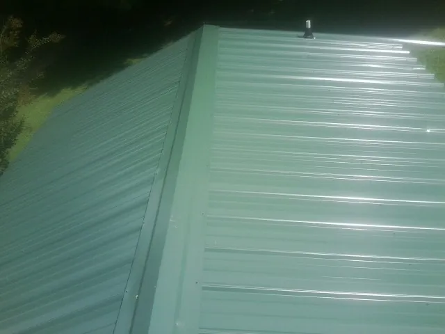 New green metal panels meeting at the ridge of a roof — Flat Roof Repair work by our crew in Petros