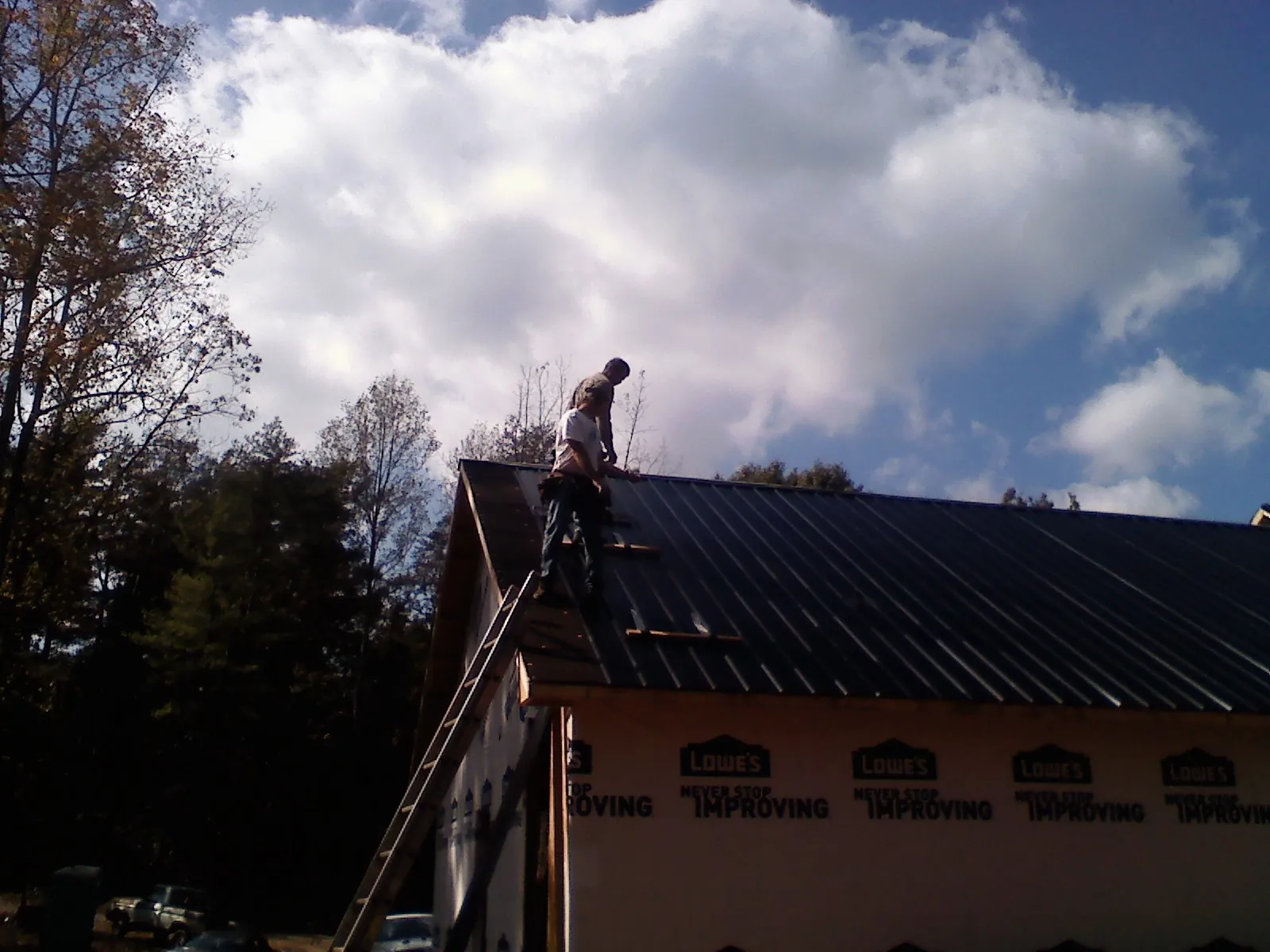 Roofer fastening dark metal panels high against a cloudy sky, from a Roof Inspection job in Petros