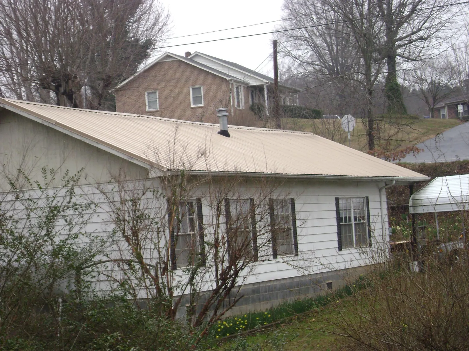 Tan metal roof on a white sided house set into a hillside — Commercial Roofing by Roofing Brothers in Petros